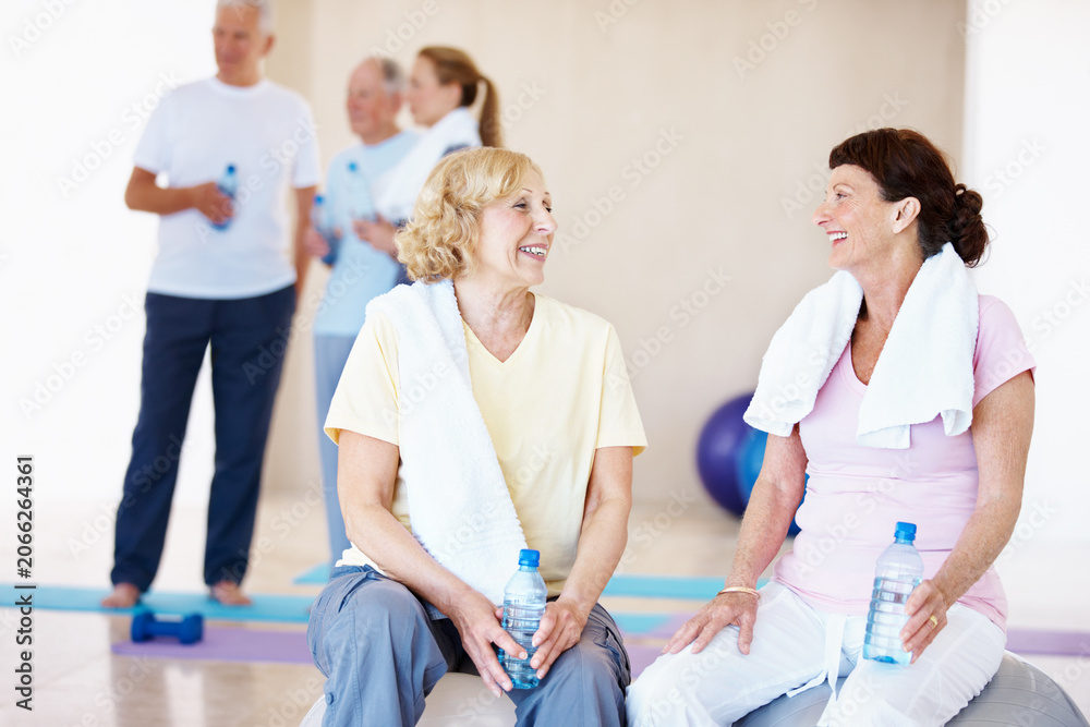 Naklejka premium Fitness, happy or old women in class with break, cardio rest or bonding in workout hobby. Smile, cool down or friends in center with water bottle, team connection or recovery in retirement training.