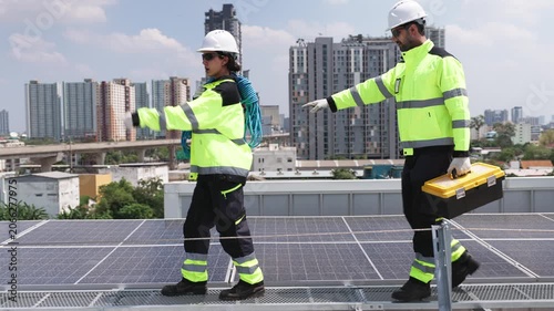 Two solar technicians installing and securing photovoltaic panels on a rooftop solar energy system in an urban environment.