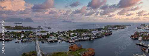 Schilderij op canvas Aerial view shows Svolvaer and Henningsvaer in Lofoten, Norway, with rocky islets, harbors of wooden houses, a bridge over calm fjord waters, and soft evening light