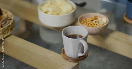 Camera is pulling back rising revealing ribbed mug on coaster chips snacks and remote showing setup