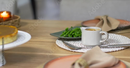 Camera is starting slow pass across wooden dining table, highlighting espresso cup and green beans