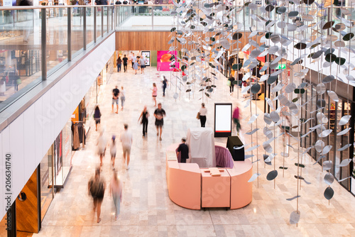 ground floor of large shopping centre, with retail stores, kiosk, blurred shoppers