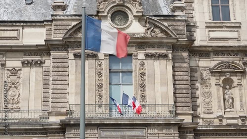 French flag waves on pole outside Louvre palace building in Paris France. National tricolor banner concept for european politics government news and french state holiday celebration.