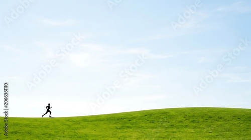 A lone runner traverses a vast, undulating green hill under a clear, expansive blue sky, symbolizing freedom and the joy of outdoor exercise.
