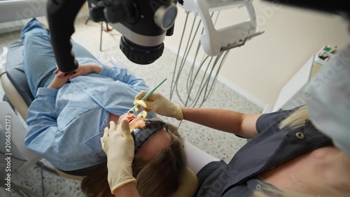 Female dentist looking through dental microscope during treatment in clinic. Concept of modern dentistry and medical technology.
