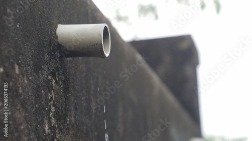 PVC pipe protruding from dark mossy concrete wall with water dripping drops leaking drainage outdoor urban detail