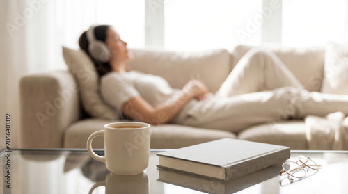 Woman relaxing on sofa with headphones drinking coffee reading book at home in peaceful lifestyle leisure atmosphere.