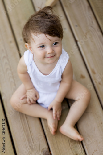 High angle portrait of a smiling toddler sitting on a wooden deck, looking up.