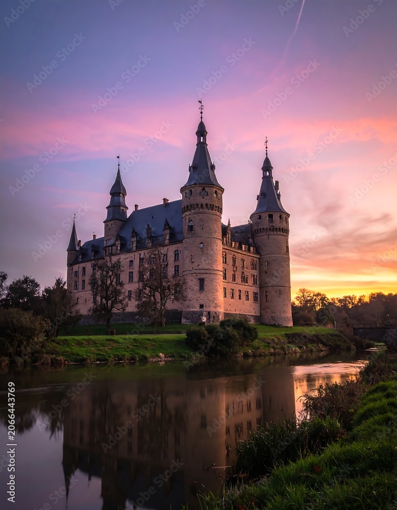 Fototapeta premium Historic castle illuminated by vibrant sunset sky reflected in tranquil water