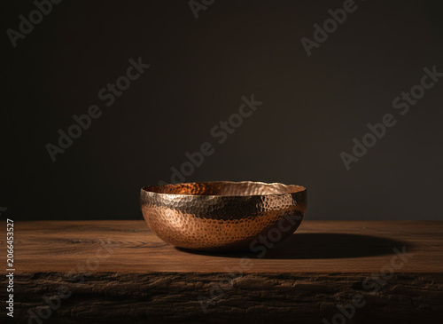 Hammered metal bowl with warm copper patina on wooden table evoking wabi sabi and artisan craft lighting casts soft shadow and rustic mood