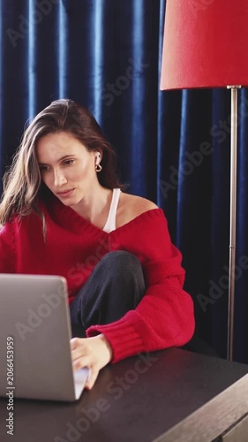 Focused and slightly tired young woman in red sweater working on a laptop, professional remote work concept, cozy home office interior, freelancer lifestyle, authentic video.