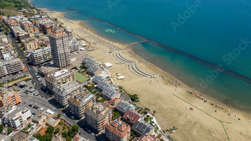 Photos Aerial view of Nettuno coastline featuring the iconic skyscraper, sandy Scacciapensieri beach with umbrellas, seaside residential buildings, and the Mediterranean sea