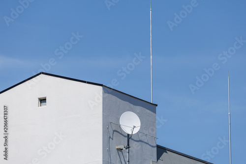 Φωτογραφία Conceptual scene: white satellite dish and antenna mast on a minimalist white building corner lit by a sharp diagonal sunlight band, showcasing modernity’s reliance on invisible systems