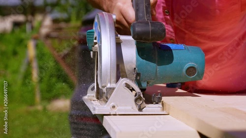 Carpenter Cutting Wooden Board with Circular Saw Outdoors