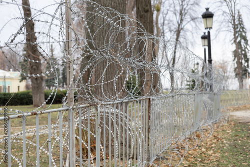 Foto Coils of razor wire atop a metal park fence, creating a barrier in a public outd