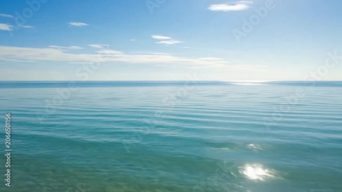 Calm turquoise ocean water under a clear blue sky with soft white clouds
