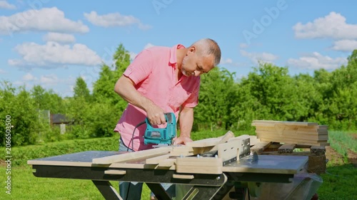 Carpenter Using Electric Jigsaw to Cut Wooden Boards Outdoors