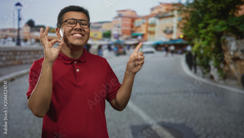 Tableau sur toile Hispanic man wearing glasses and red polo making ok sign with hand and pointing finger on street; confidence optimism joy