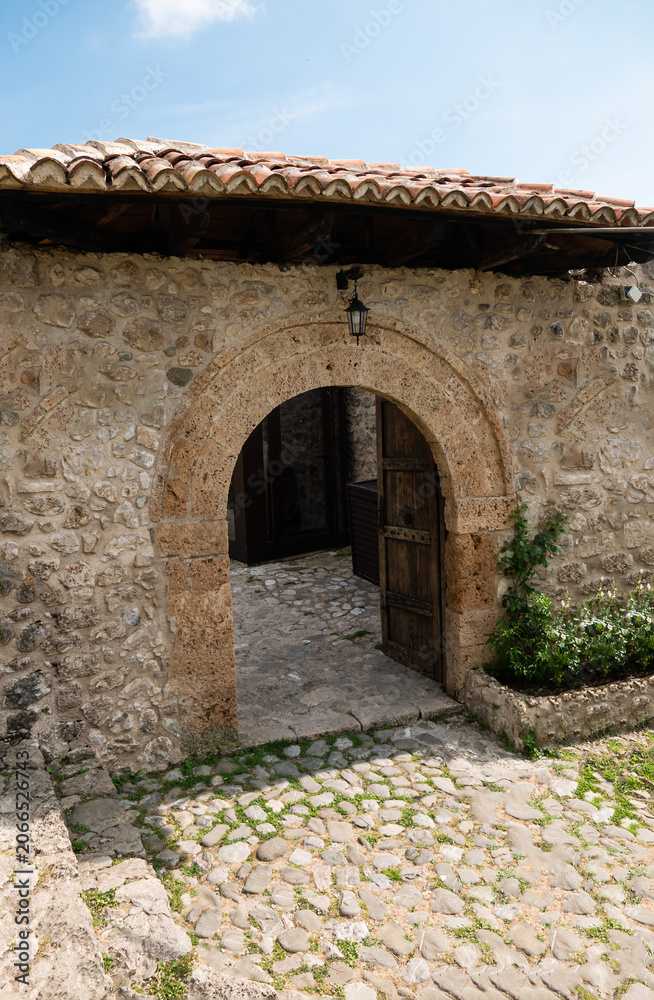 Obraz premium Historic stone arch entrance with rustic wooden door in medieval architecture courtyard.