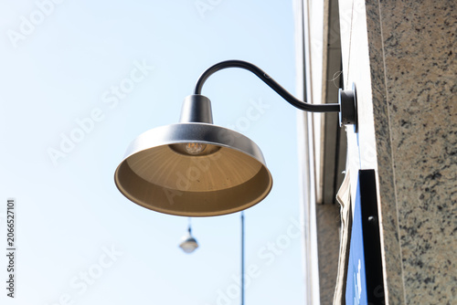 Slika na platnu Close-up of a modern metallic gooseneck wall lamp mounted on a stone building facade against a clear blue sky