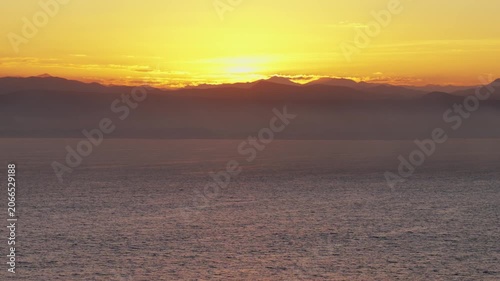 Sunset over calm ocean with distant mountain horizon, copy space