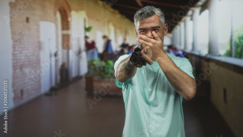 Fotografie Man pointing finger and covering mouth with hand in a corridor of a historic building, visible archways and columns; embarrassment apology regret