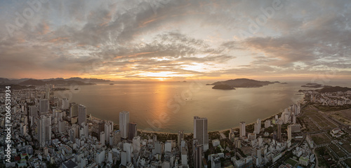 Panoramic sunrise over Nha Trang Bay with dense urban skyline, golden reflection on water, and islands along the coast.