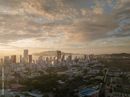 Early morning aerial view of Nha Trang urban center with modern towers, dramatic clouds, and surrounding mountains.