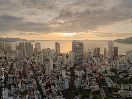 Golden sunrise light over Nha Trang city center featuring dense urban buildings, coastal bay, and distant islands.