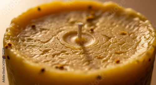 A close-up photo of a textured handmade yellow beeswax candle showing a warm, rustic surface and a single central wick