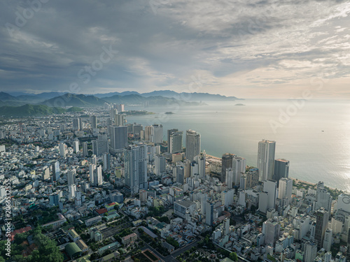 High altitude aerial perspective of Nha Trang beachfront skyline with calm sea, mountain backdrop, and modern development.