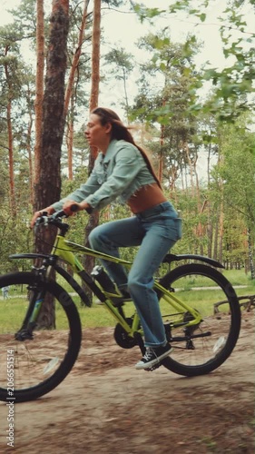 Young woman enjoys a peaceful ride on a mountain bike through a scenic forest trail, surrounded by tall pine trees and summer greenery.