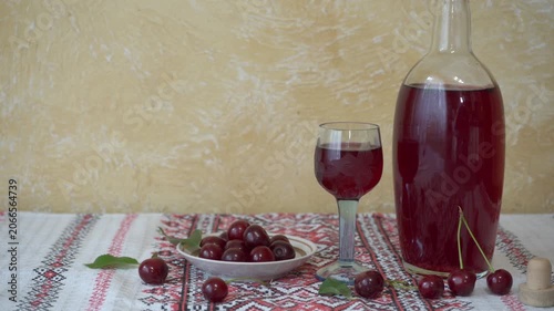 Traditional homemade cherry liqueur in a bottle and glass on an embroidered tablecloth. Homemade cherry infused alcohol next to a plate of fresh berries