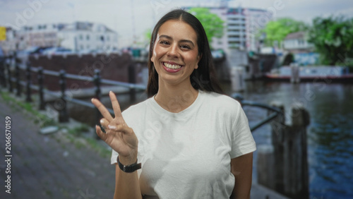 Canvas Print Woman young brunette smiling with thumbs up at a canal street in amsterdam wearing white t shirt and watch; joy approval