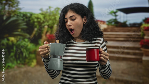 Fotografija Woman holding red mug and stovetop coffee pot with open mouth on building steps; surprise coffee morning routine