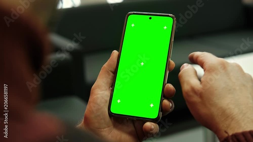 Man holding smartphone with green screen and tracking markers close up over shoulder view. Mobile phone mockup display chroma key space for application web template. Digital device usage
