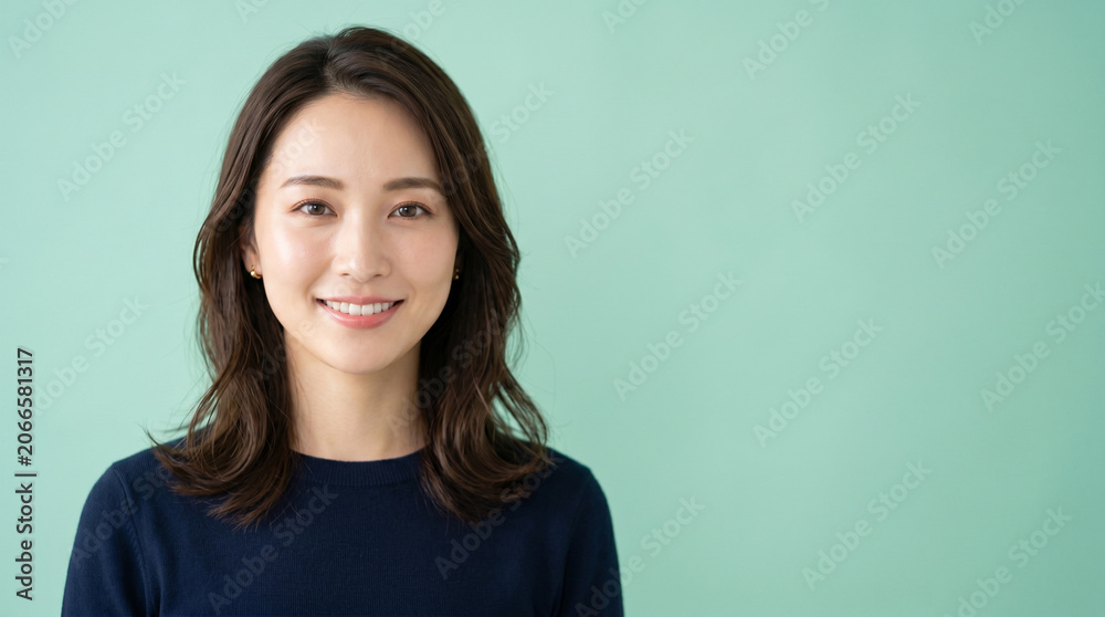 Fototapeta premium ミントグリーンの背景で微笑む女性を描いたライフスタイルイメージです。 清潔感のある表情が美容や健康、ビジネスシーンにも活用しやすい印象を与えます。