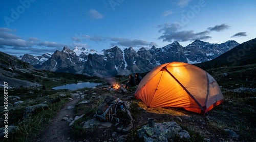Camping tent glowing at twilight by mountain lake in wilderness  