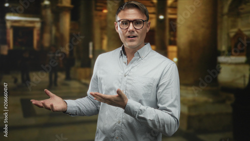 Konstfotografi Man with glasses and white shirt gesturing open hands and speaking in a cathedral interior with marble columns and altar; reflection