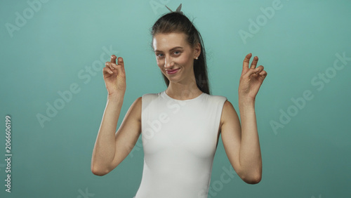 Cuadro en lienzo Young woman in white sleeveless top making air quotes with both hands and slight smile in teal studio; playful irony