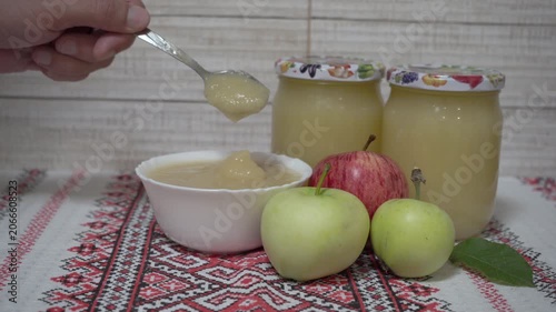 Glass jars of applesauce and fresh apples, tasting apple jam from a spoon, close-up.