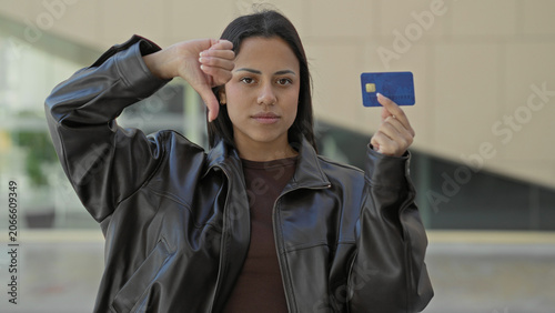 Fotografia Woman holds creditcard with right hand and shows thumbs down gesture in building entrance; consumer distrust