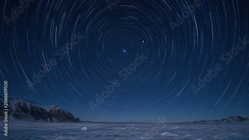 Arctic night sky with star trails circling a bright Polaris star in dark blue tones. 