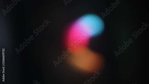 This video clip features a dynamic and smooth movement of abstract, out-of-focus light shapes in vibrant blue, pink, orange, and yellow against a dark background.