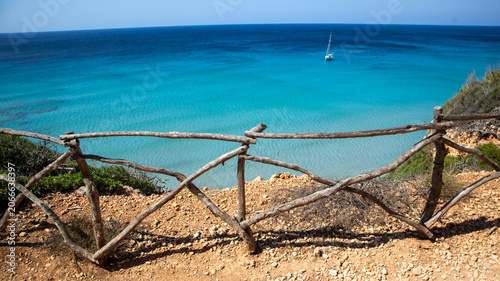 Wooden fence overlooking a turquoise sea with a sailboat