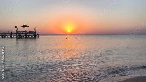 Rising vivid colorful sun, calm ocean surface with small waves and pier. Distant vivid sky, sea and the sunrise. Sun, bay and water with the buoys, landscape travel photography. 
