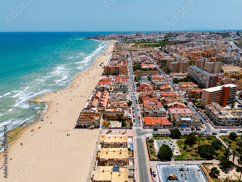 Aerial view of coastal town with sandy beach and breaking waves in Mediterranean Sea. La Mata, coastal tourism, vacation destination, travel. Costa Blanca, Spain