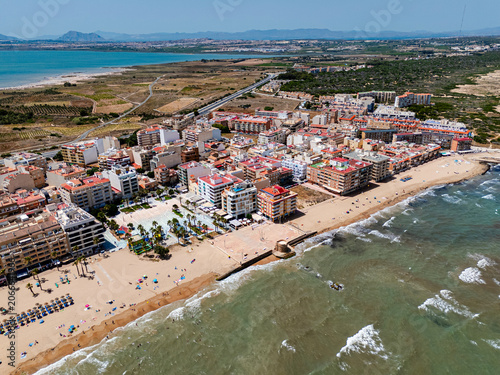 Aerial view of coastal town with sandy beaches, residential buildings, and Mediterranean Sea. Coastal tourism and vacation destination concept for travel advertising. La Mata town, Costa Blanca, Spain