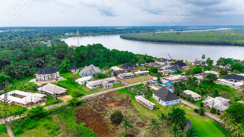 Aerial view of a residential settlement nestled along a riverbank with lush green vegetation, scattered houses, and dirt roads in Minima, Rivers, Nigeria.