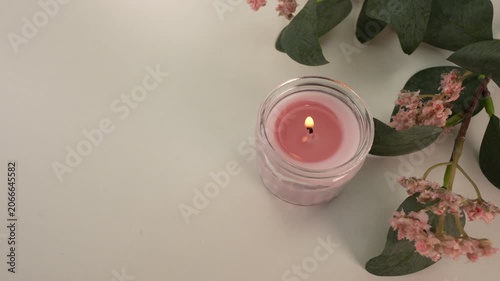 Burning candle and pink flowers on white table. Top view.